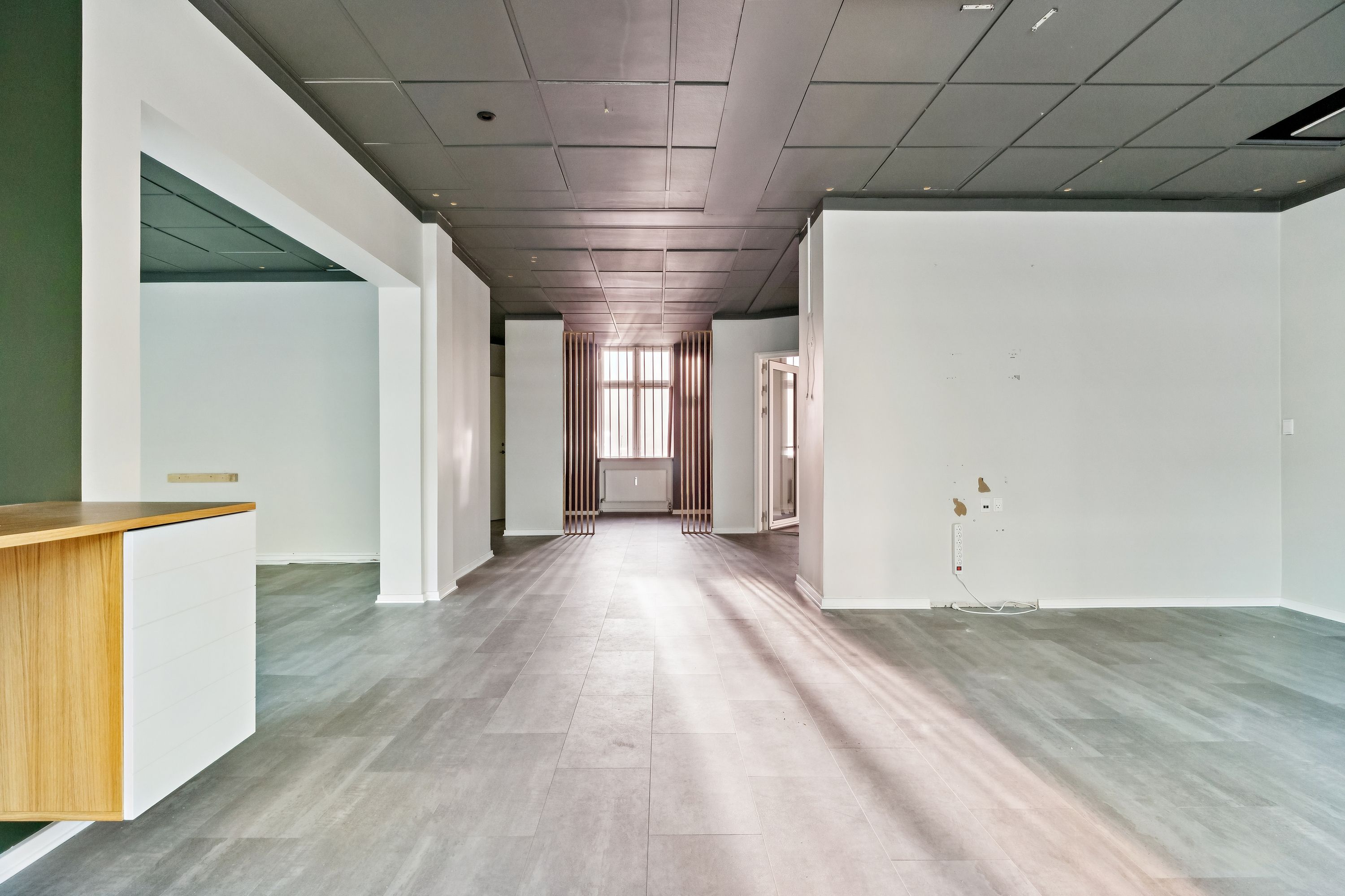 Store tomrum med hvide vægge og lysegule gulve, åbne døre og vindu og radiatorer i baggrunden