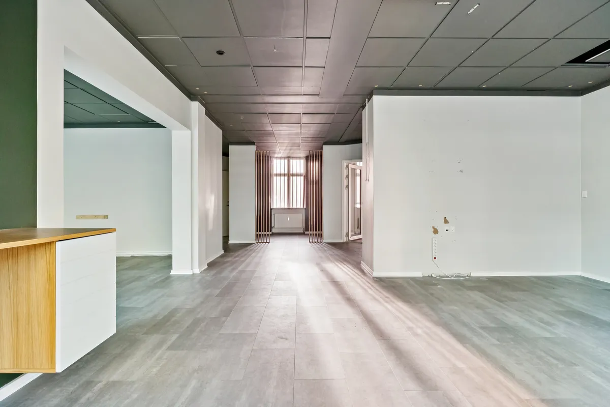 Store tomrum med hvide vægge og lysegule gulve, åbne døre og vindu og radiatorer i baggrunden