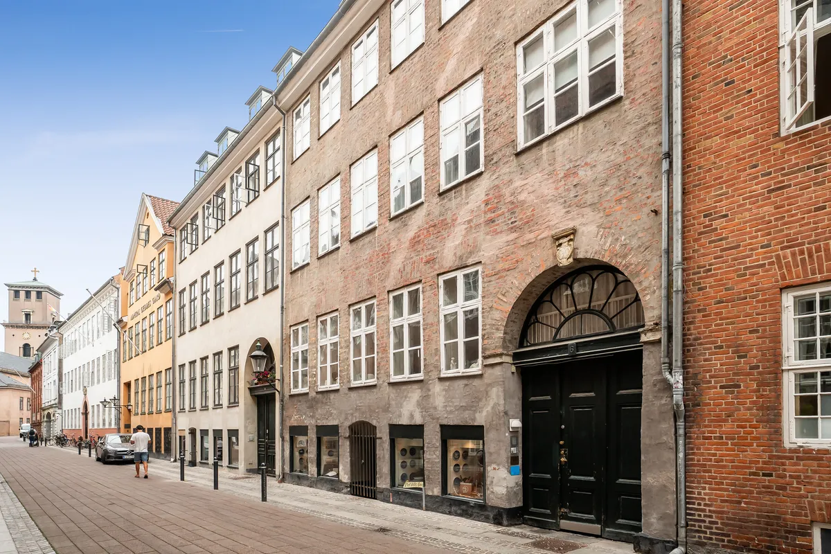 Kontor til leje på Store Kannikestræde 6B. Bygningen har mange vinduer og en stor hoveddør. En person går forbi. I baggrunden er der en kirke.