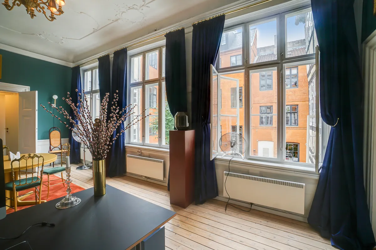 Kontor med store vinduer, lysegul væg og møbler med moderne og klassisk design, gulvtæppe, lysekroner og plante i vase