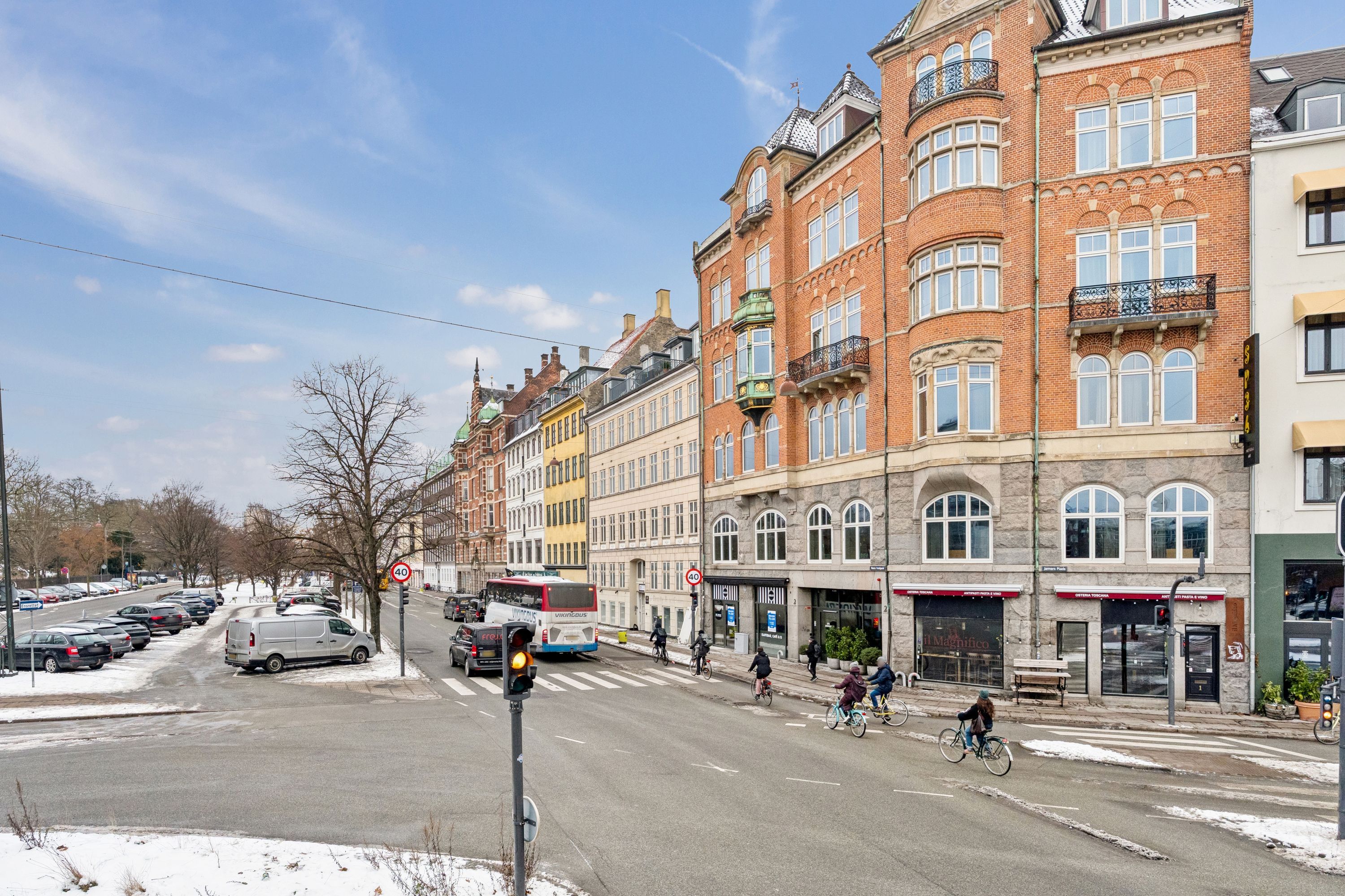 Cyklister kører gennem en krydsning med stoplys på en hårdfør, koldt vinterdag med sne og bus og biler på en trafikeret gade i København