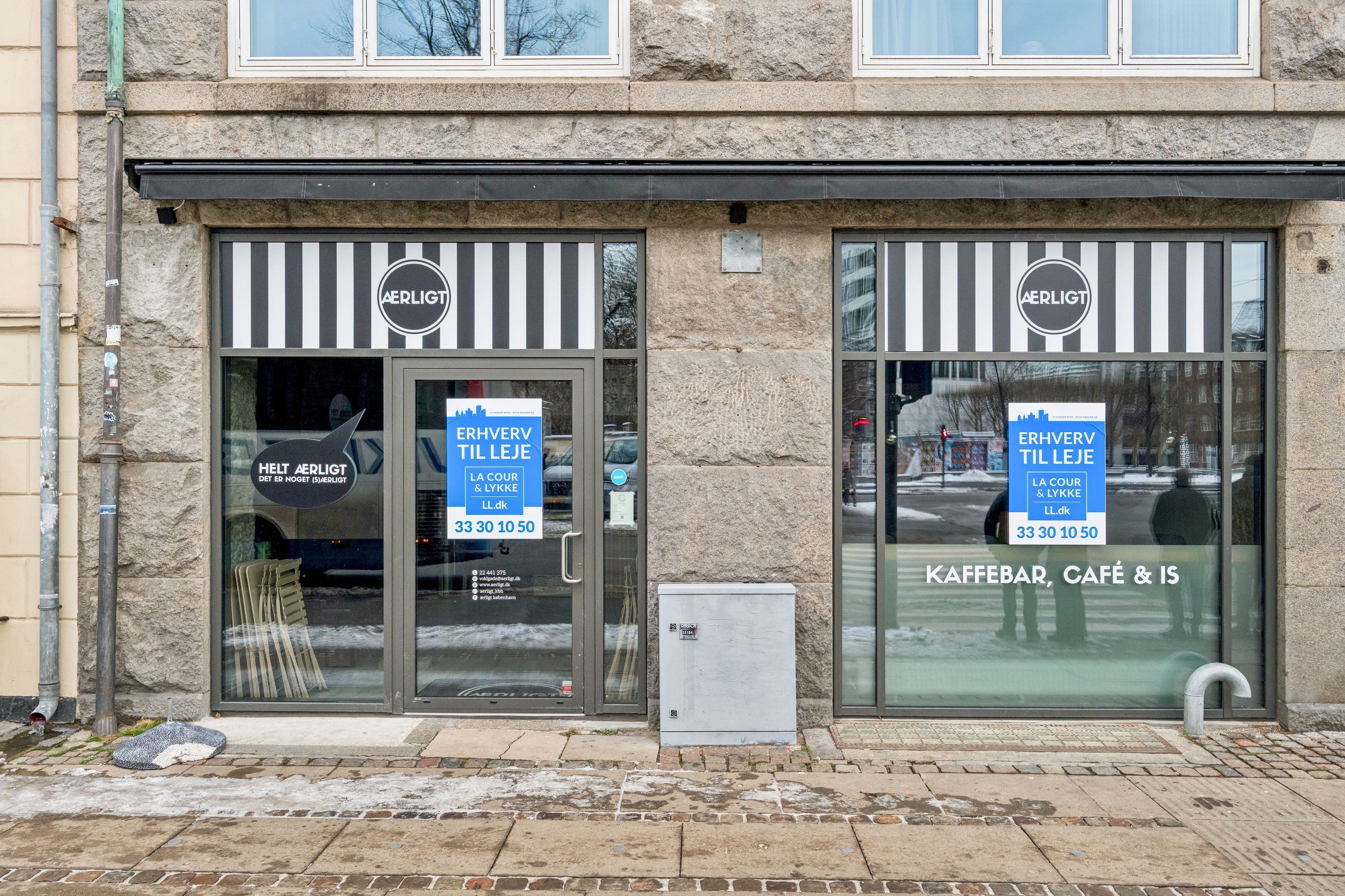Foto af facaden til cafeen Aerligt på Nørre Voldgade 2, København K med skilte, der viser åbningstider og opfordrer til leje. Der er skrift på skiltet i blåt og sort med et logo på samme farve.