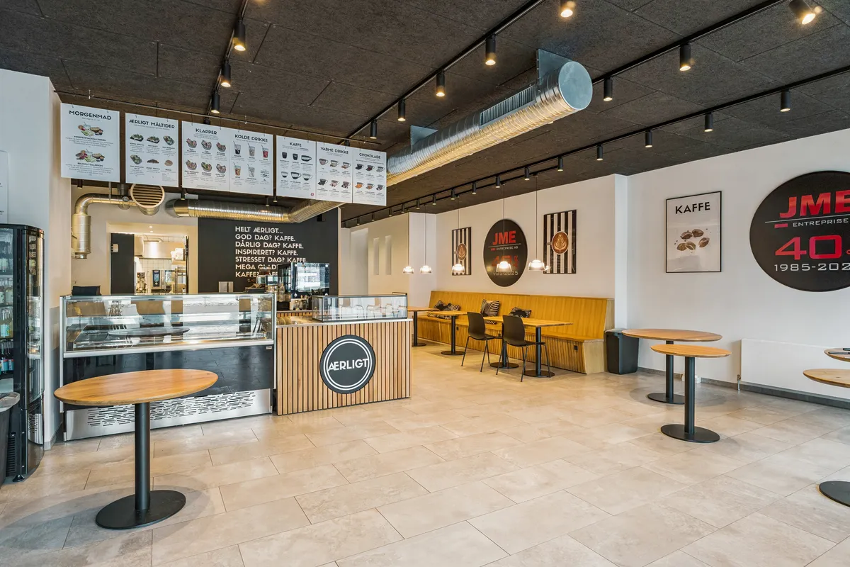 Lyserødt og hvidt caféinteriør med runde borde, lysekroner, stolpelampe, menukort, udlejningsreklame og hvid gulvbeklædning