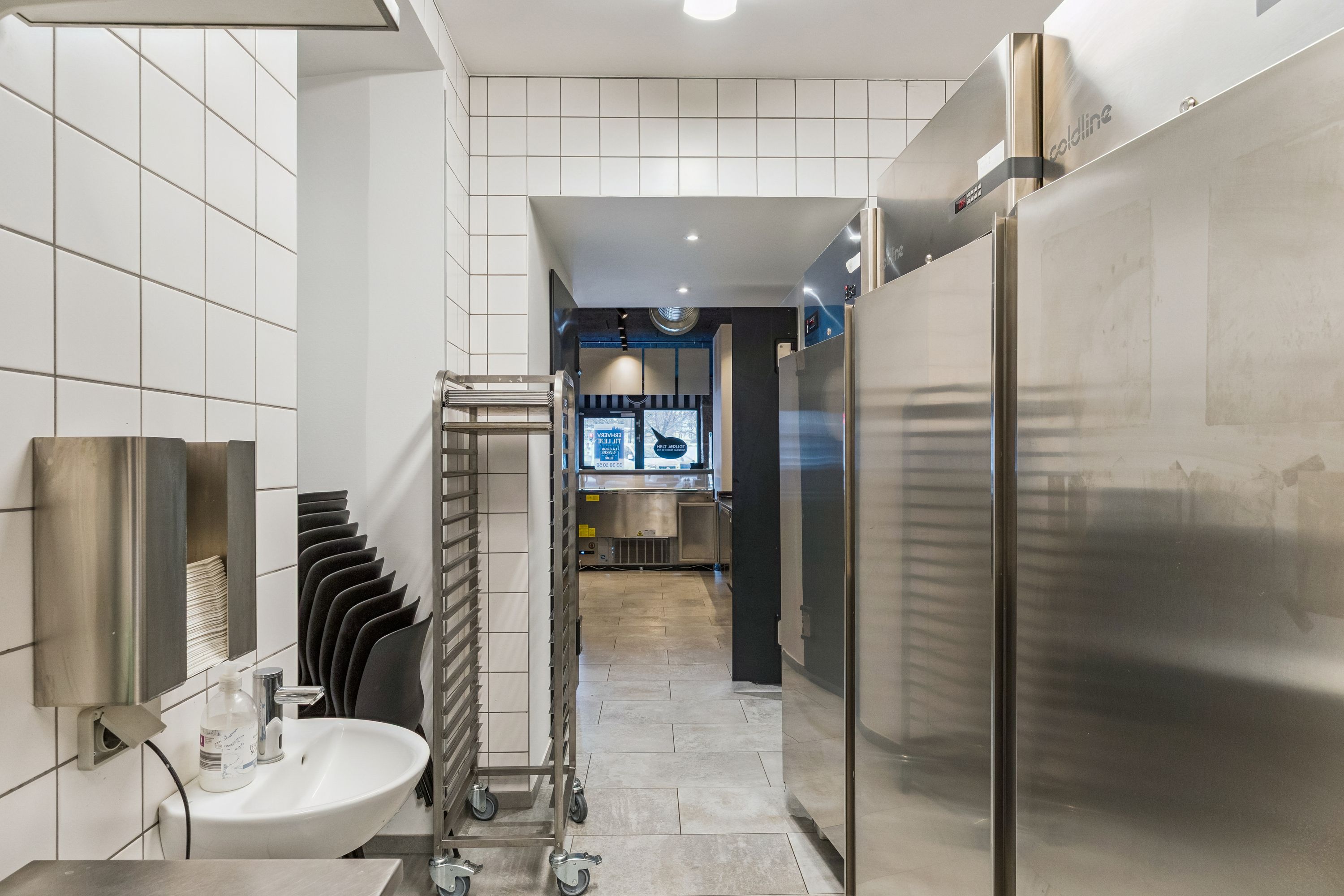 Bag et længesvindende køkken med stålkøleskabe og renlighedsstandarder i et kommercielt lokale med en funktionel håndvask og et køkken med flere udstyrselementer
