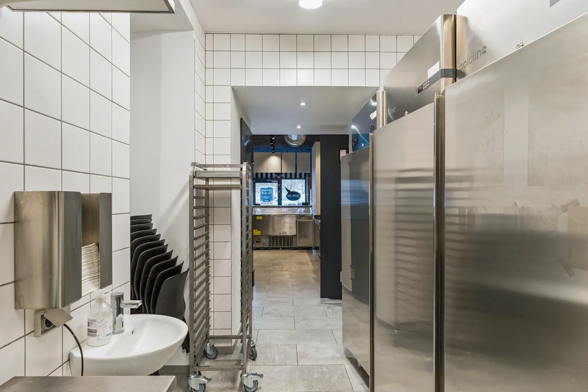 Bag et længesvindende køkken med stålkøleskabe og renlighedsstandarder i et kommercielt lokale med en funktionel håndvask og et køkken med flere udstyrselementer