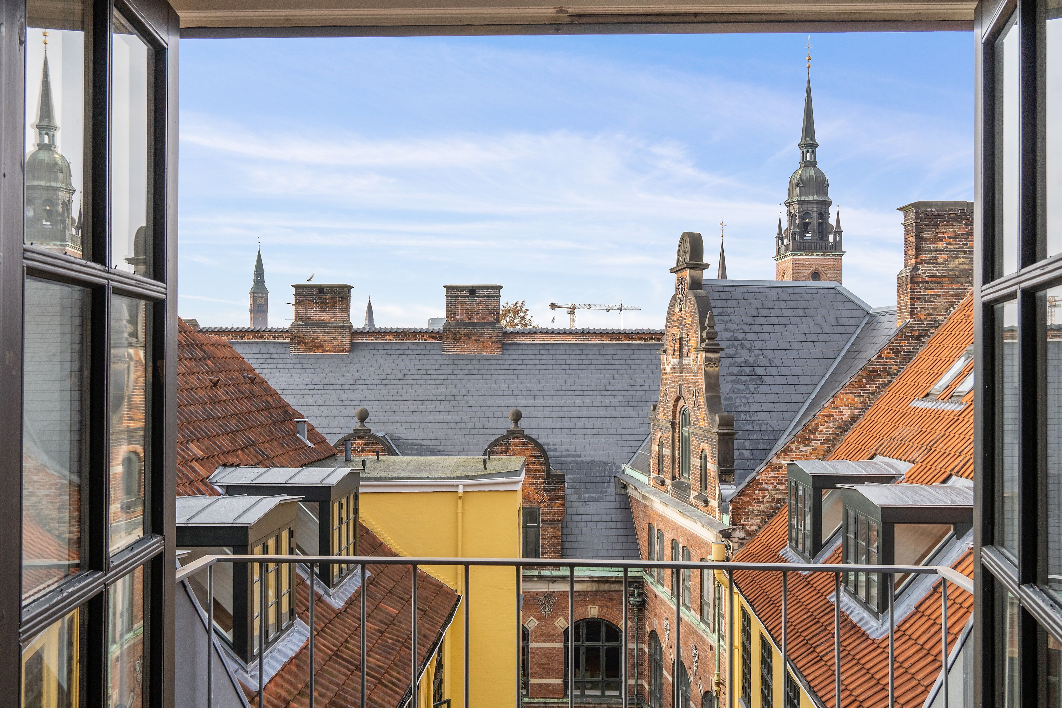 Moderne kontor med udsigt over Københavns røde tagdækninger og spir. Kontoret har gulv til loft og store vinduer til gaden.