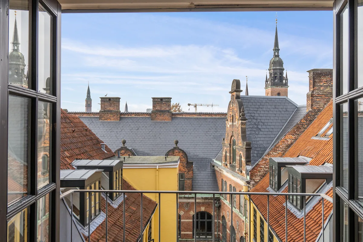 Moderne kontor med udsigt over Københavns røde tagdækninger og spir. Kontoret har gulv til loft og store vinduer til gaden.