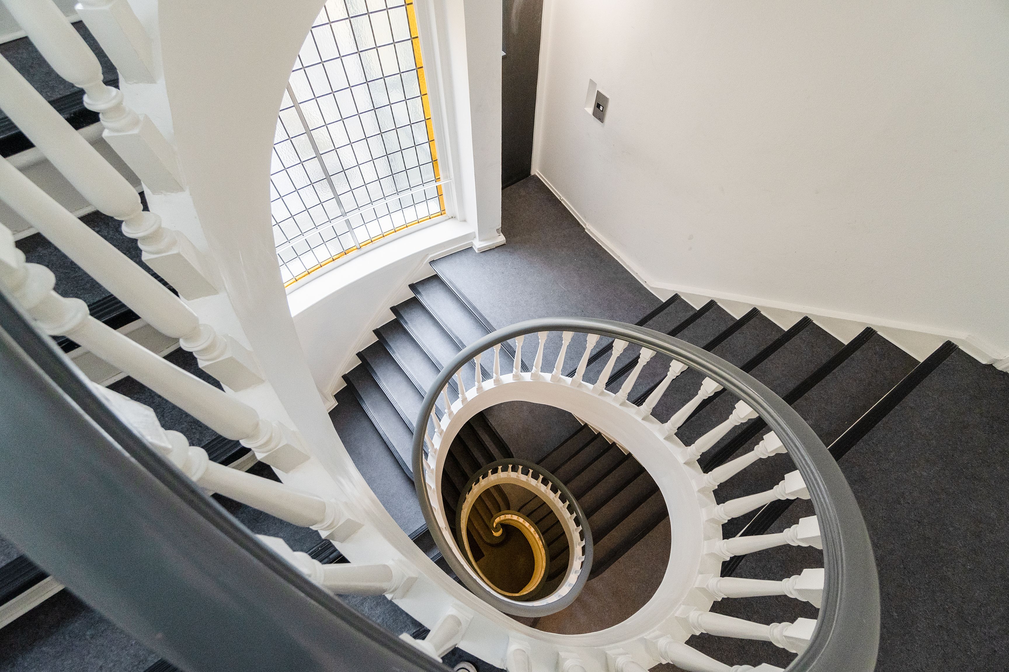 Rund trappe i moderne kontor med hvide og grå farver og lyseglas i gul bue