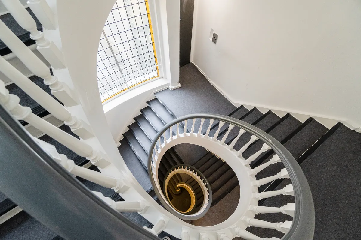 Rund trappe i moderne kontor med hvide og grå farver og lyseglas i gul bue