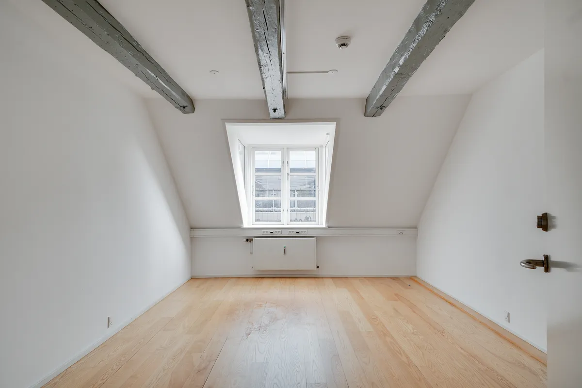 Lej kontor i lyse loftsrum med hvide vægge og trægulv i København. Rummet har lyse træbjælker, lys og vinduer og et hvidt radiatorsystem