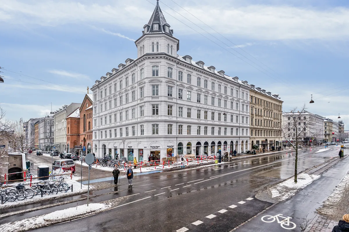 Vinduet med skiltet Flying Tiger på Frederiksborggade 23. Allerede flere mennesker går forbi på vejen med sne. Langs gaden er der flere bygninger og træer.