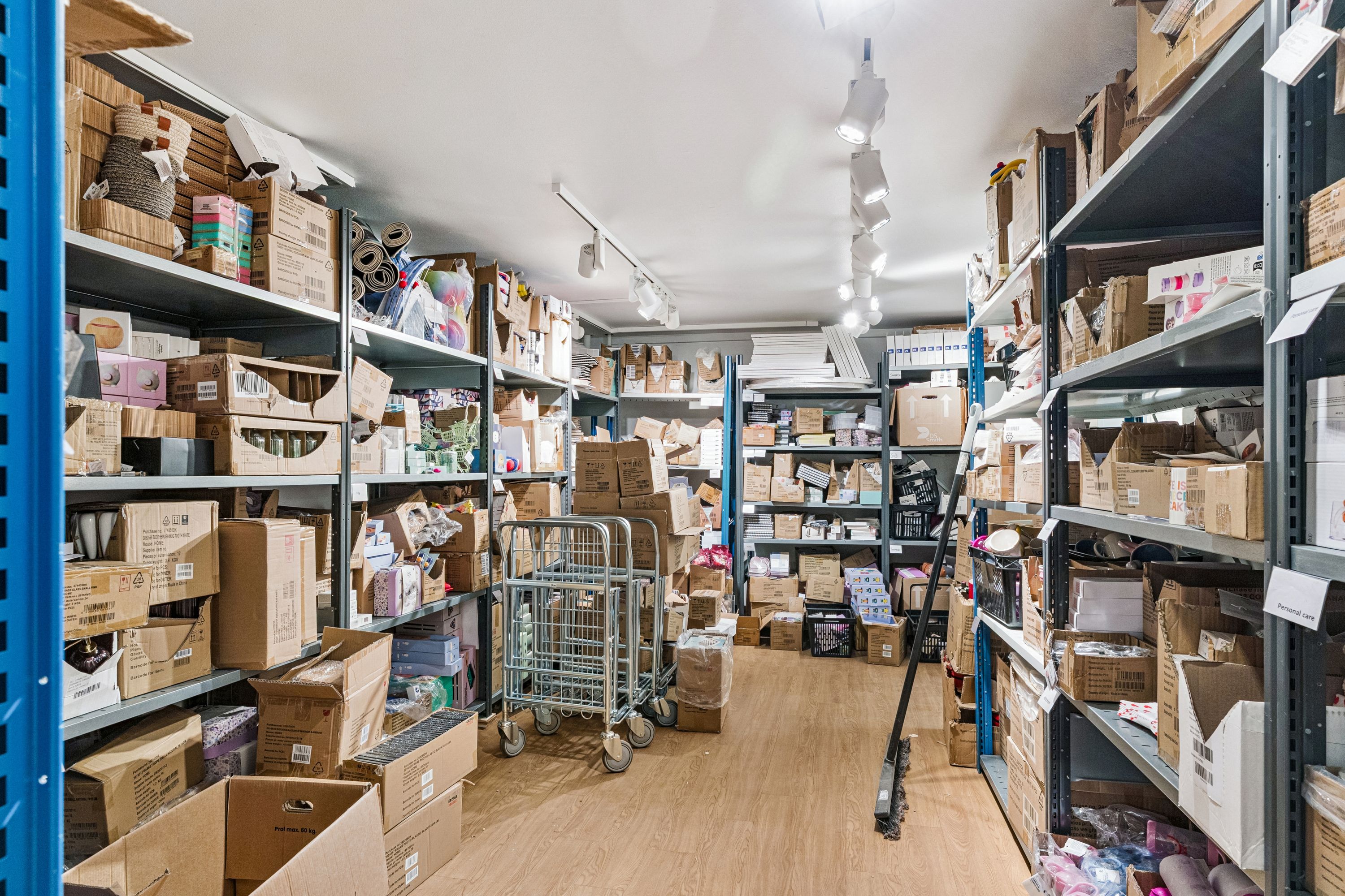 En stor lagerhal med hylder fyldte med kartoner og kasserne samt to stålvognskurve på gulvet