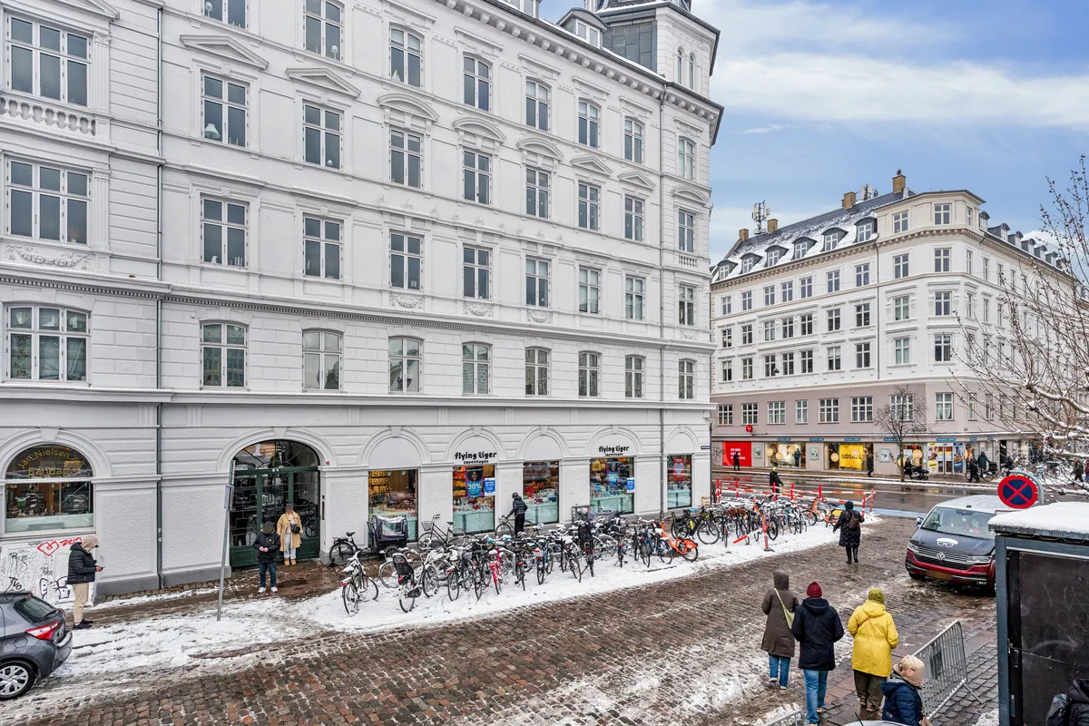 Folk går i snede gader med sne omkring, og folk går forbi en butik med navnet Flying Tiger og mange cykler parkeret udenfor