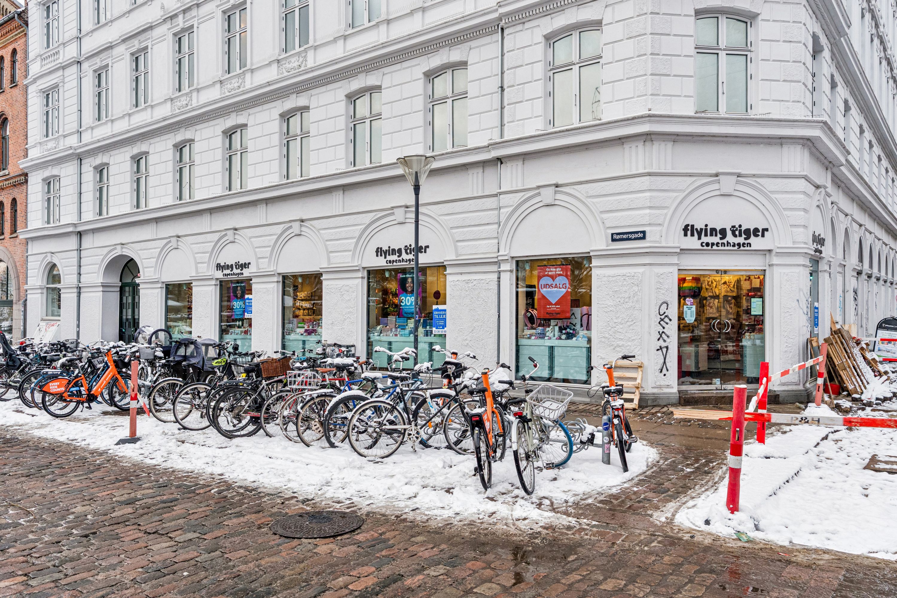 Butiksforretning med Flying Tiger på Frederiksborggade i København med flere cykler parkeret foran og sne på jorden