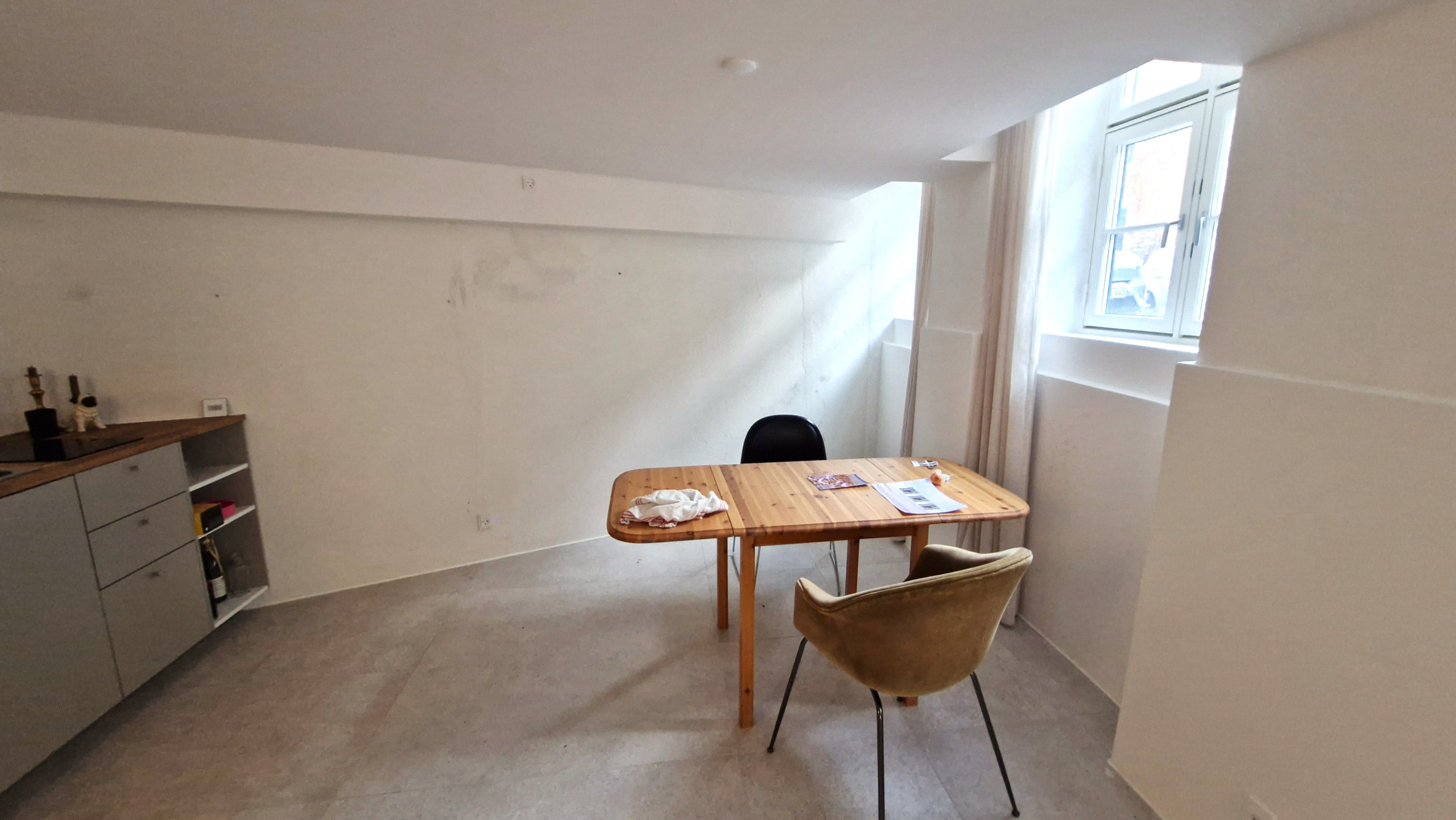 På billedet ses et rum med en bord, to stole, et vinglas og en flaske på hylde. Rummet er rent og velholdt.