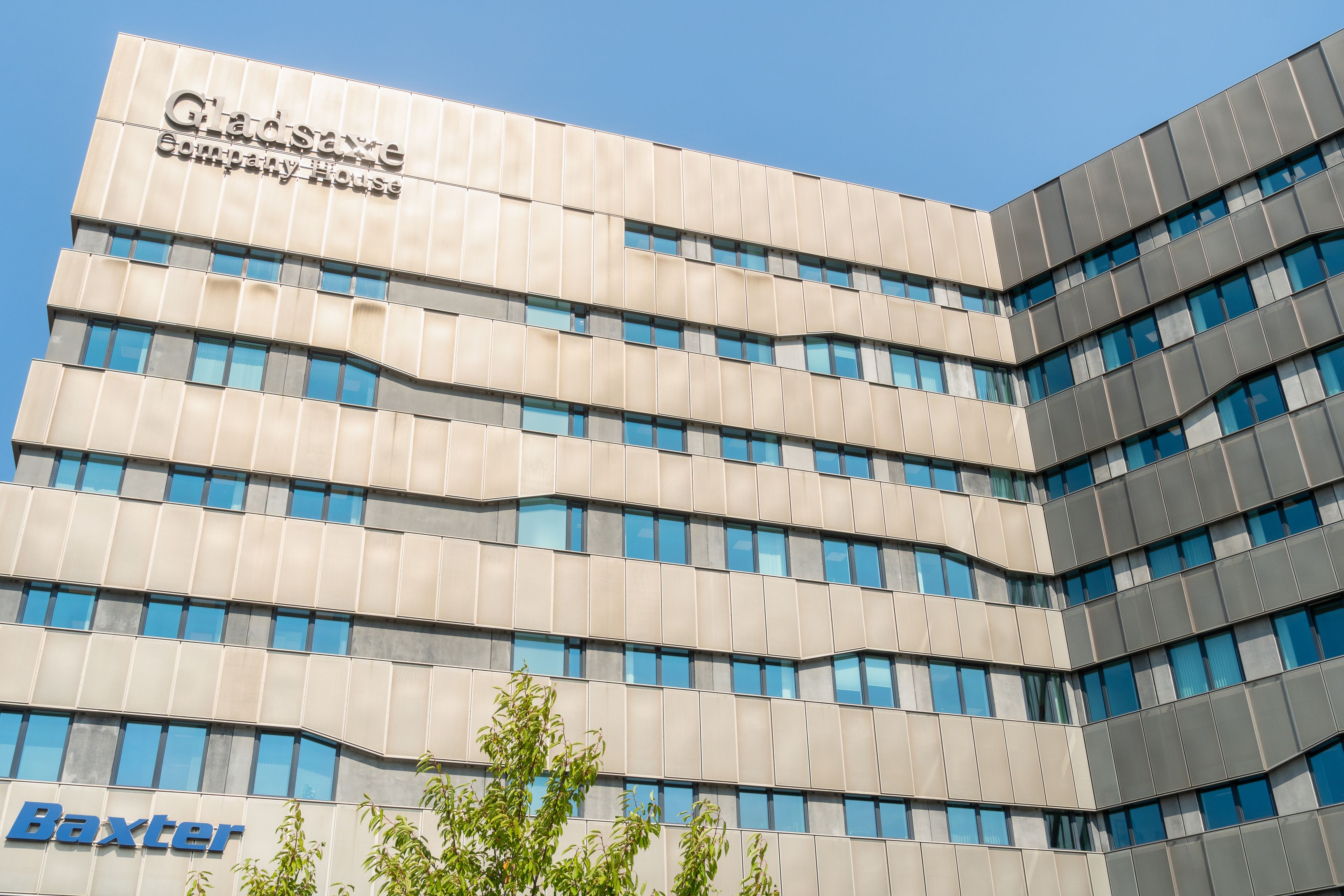 Gladsaxe Company House med lyse vinduer og en klar himmel bagved. Bygningen har en gul facade og teksten Baxter og Gladsaxe Company House.