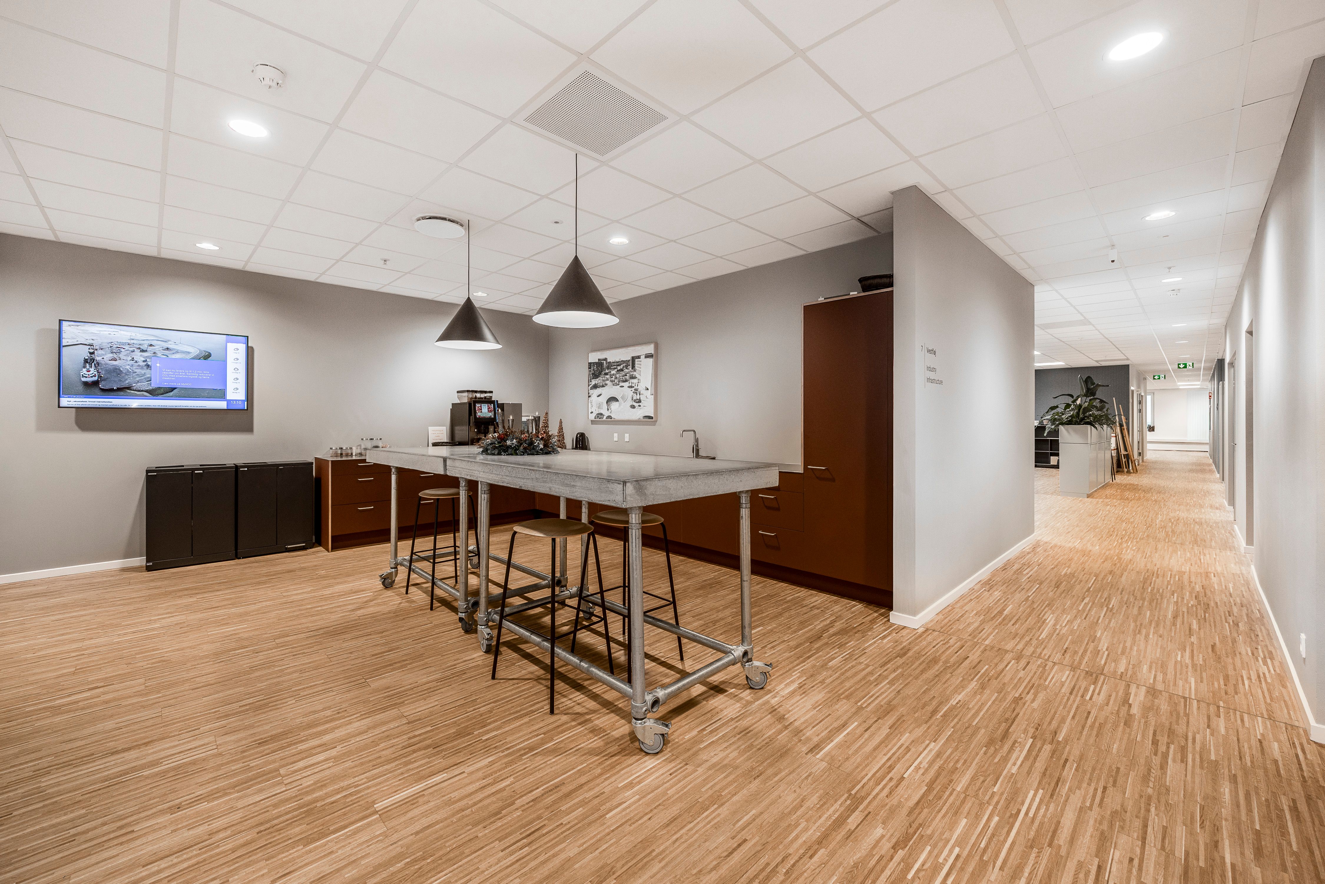 Moderne kontor med høj service og fællesfaciliteter på Tobaksvejen 2A, 5. sal i Søborg. Elegant kantine med marmorbord, stolpelamp og tv-skærm samt brun skab og plante.