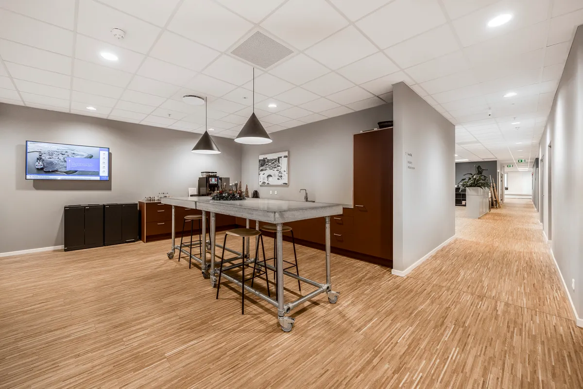 Moderne kontor med høj service og fællesfaciliteter på Tobaksvejen 2A, 5. sal i Søborg. Elegant kantine med marmorbord, stolpelamp og tv-skærm samt brun skab og plante.