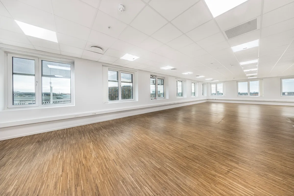 Stille kontorrum med højt til loftet, lyse loftslampe og trægulv samt vinduer med udsigt over byen