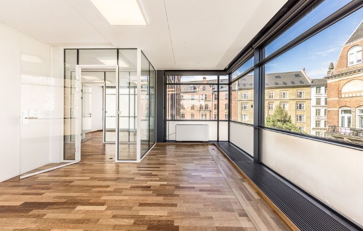 Kontor i ikonisk miniskyskraber på Nørrebro med flisede gulve og store glasvinduer med udsigt til bygning med røde mursten og træterrasser.