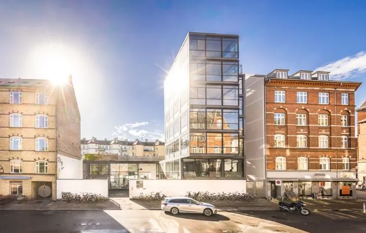 Solskin i skyskraber, parkerede biler og motorcykler, glasvinduer, og et forretningscenter på Nørrebro