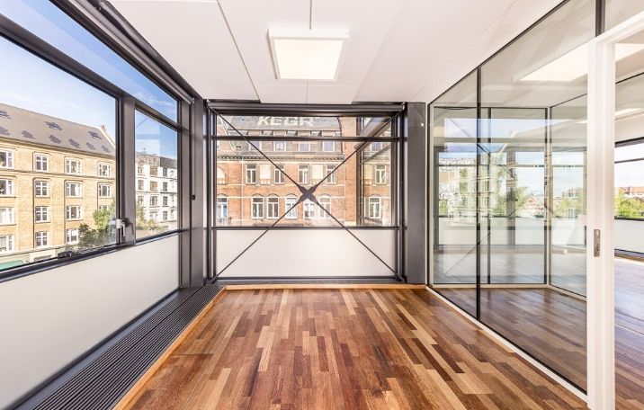 Minimalistisk kontor i miniskyskraber med glasvinduer, massivt trægulv og åbne rum mod gården