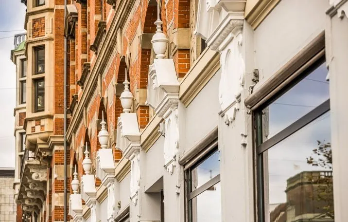 Bygning med røde mursten og hvide detaljer, med store vinduer og refleksioner af byen i glasruderne, samt hjørnemødelokale