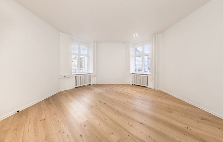 En stor, klassisk kontorbygning med hjørnerunder, hvide vægge og trægulv og flere vinduer med radiatorer nedenunder