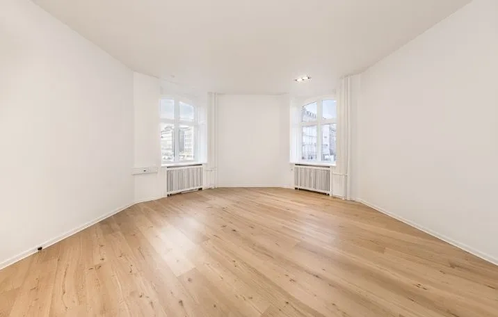 En stor, klassisk kontorbygning med hjørnerunder, hvide vægge og trægulv og flere vinduer med radiatorer nedenunder