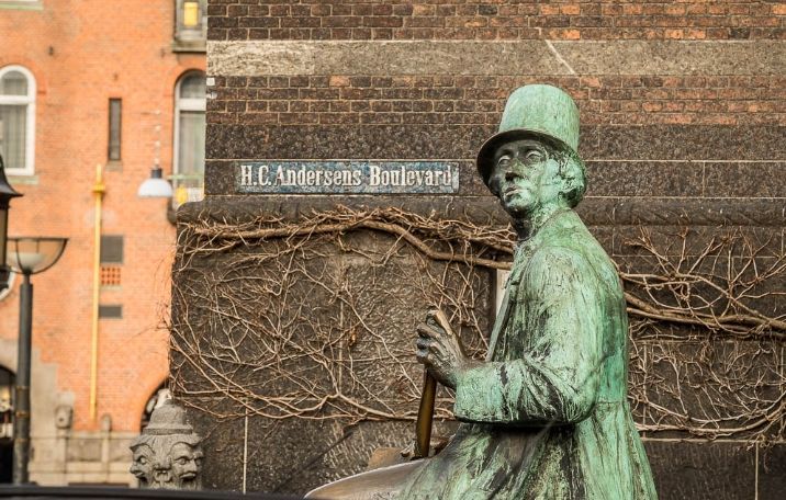 En bronzestatue af Hans Christian Andersen sidder på en terrasse med vinstokke foran en bygning med skiltet H.C. Andersens Boulevard