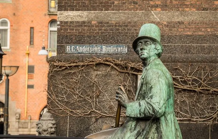 En bronzestatue af Hans Christian Andersen sidder på en terrasse med vinstokke foran en bygning med skiltet H.C. Andersens Boulevard