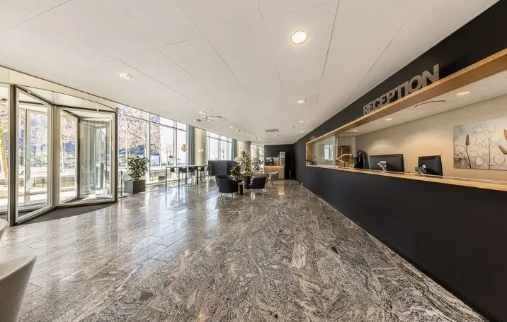 Lobby med glasdøre, marmorgulv, reception, plante og møbler i lobbyen, skrivebord med computer, stol og udendørs udsigt