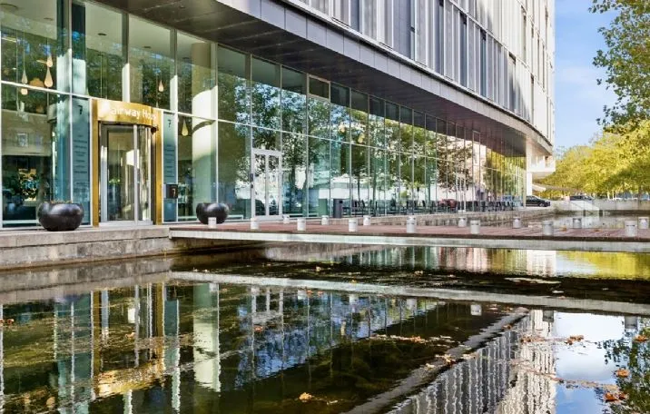 En moderne bygning med glasfassade og sø foran, samt store, sorte boliger. Et stort gult skilt med teksten "Airway Hub"