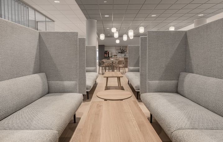 Kontor med store, mørke sæder og lyse loftslamper i en moderniseret kontorbygning med møbler i grå og lyse nuancer