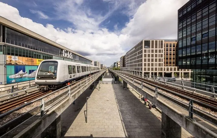 En gul og hvid metrotog kører på et skinne mellem høje bygninger i København S