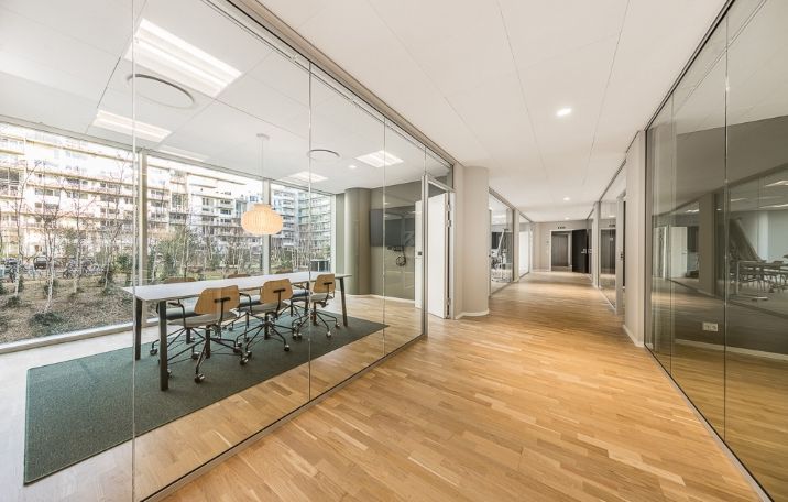 Modernt kontor med lyse lofter og store vinduer udenfor, fuldt udstyret med borde og stole