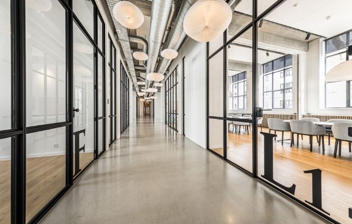 Moderne kontor med glasvægge og hvide stole og borde i en lys hall med loftslampe og trægulv