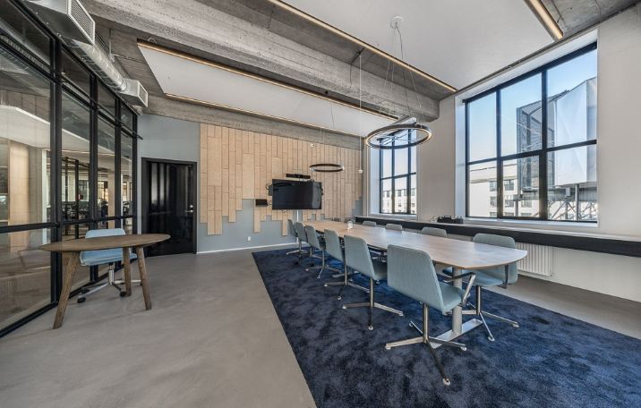 Kontorrum med runde bord, høje vinduer og moderne møbler og teknologi. Gulvtæppe og loftsbjælker for en professionel og komfortabel arbejdsplads.