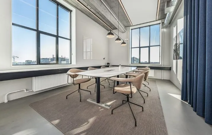 Kontor til leje med store vinduer, højloft, hvide vægge, lyse trægulve og lysekroner i lysegråt stof.