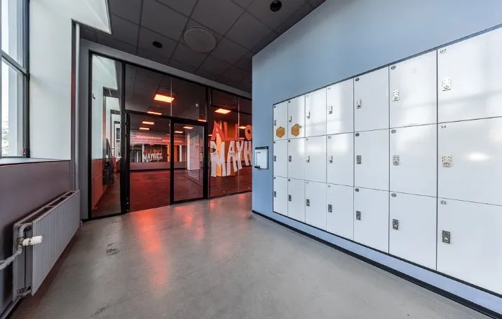 Fitnesscenter med loftsbeliggende loftsvinduer, skandinavisk design, åbne døre og tekst på væggen, samt flere skabe og en radiator mod venstre