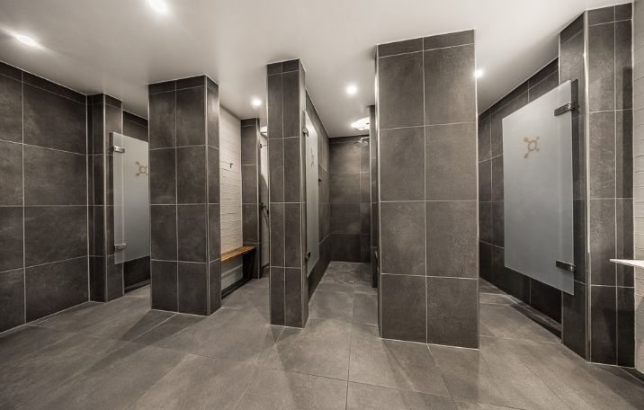 Fitnesscenter med store grå mønstre og gulv, indgange med hvide glasdøre og træbænke i en niche, ventiler og lysekroner