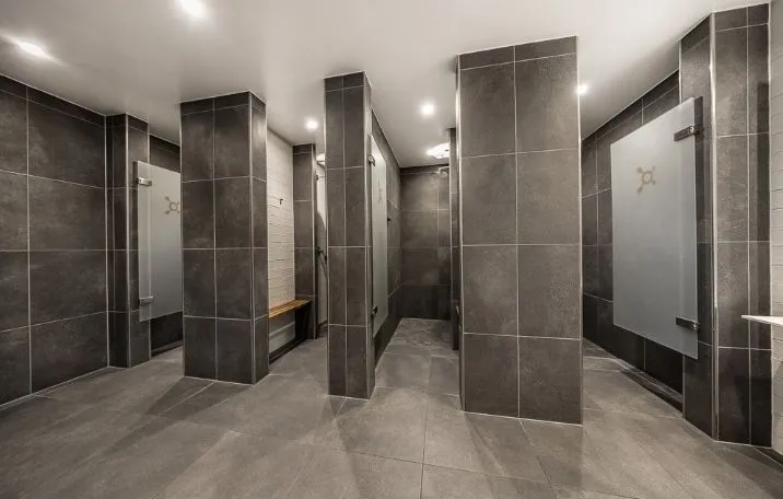 Fitnesscenter med store grå mønstre og gulv, indgange med hvide glasdøre og træbænke i en niche, ventiler og lysekroner