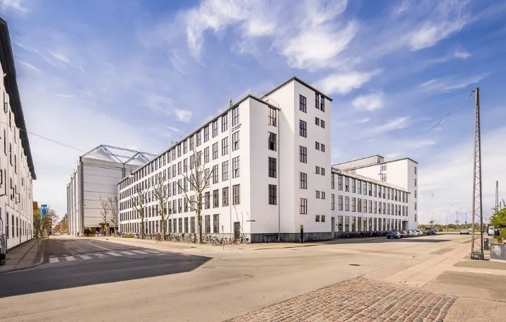 Store hvidt bygningspark med slanke høje vinduer og træer i forgrunden og biler parkeret bagved