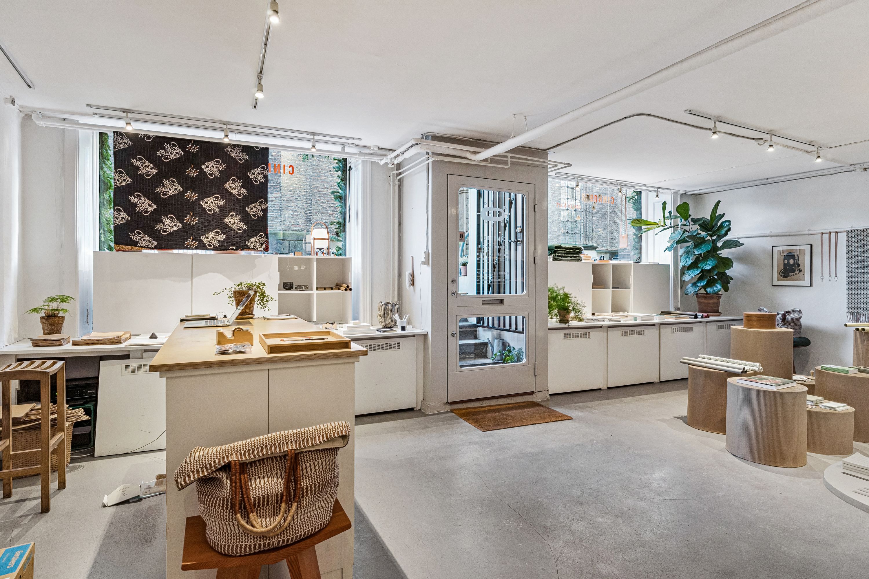 Lejlighed med højloftede rum, lyse vinduer og moderne møbler, inklusiv træbord og stol, skrivebord, læselampe og hylder med grønne planter og kunstværker