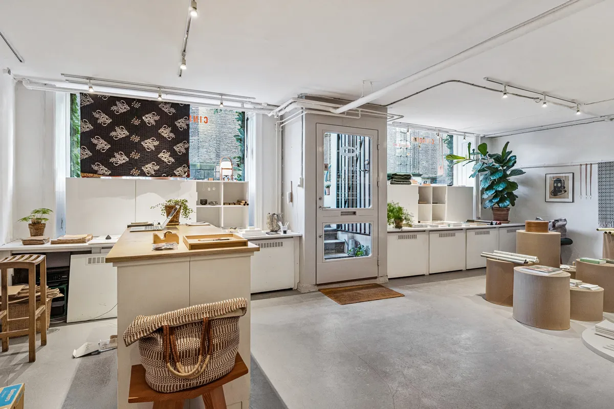 Lejlighed med højloftede rum, lyse vinduer og moderne møbler, inklusiv træbord og stol, skrivebord, læselampe og hylder med grønne planter og kunstværker