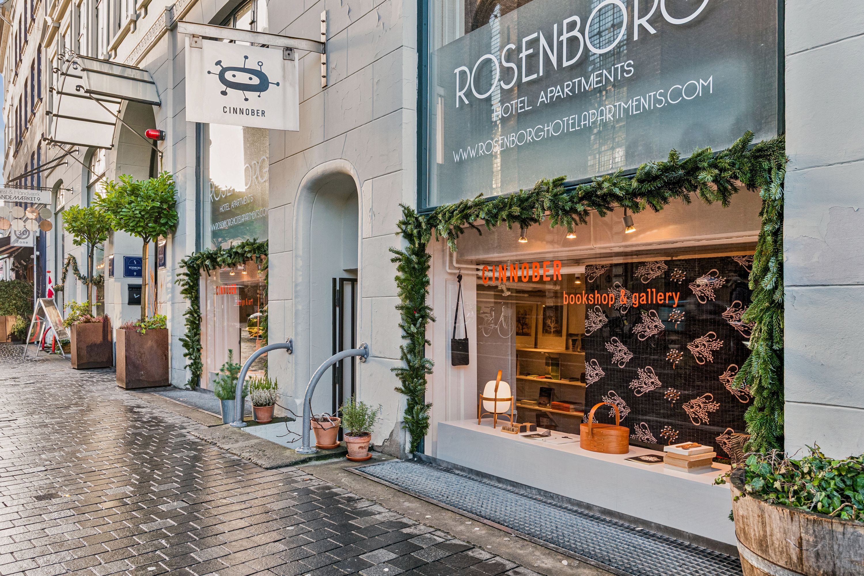 En københavnsk gade med bokse og krydderplanter. Butikken Rosenborg Hotel Apartments har en indretning med juletræer og bøger.