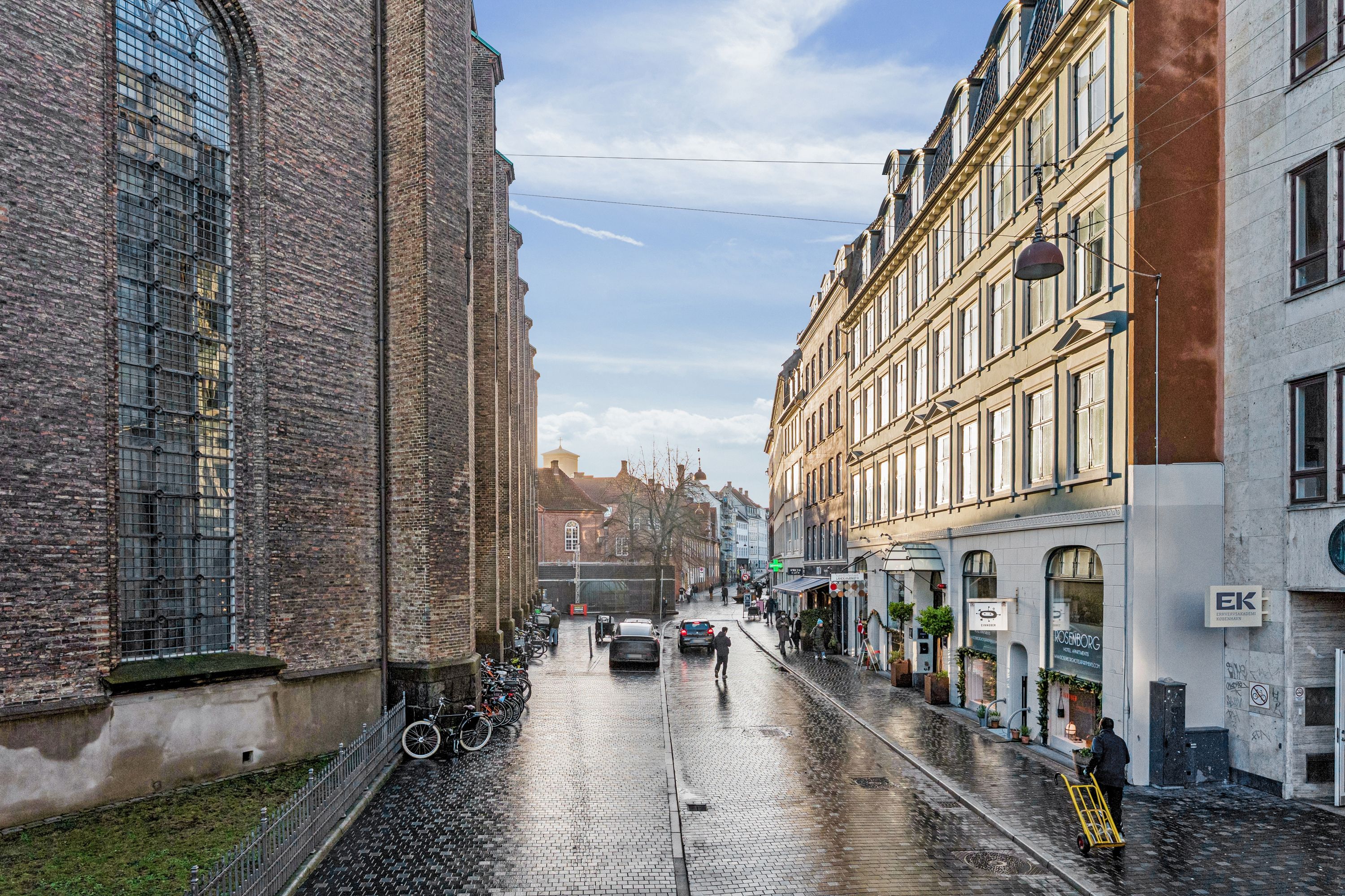 Regnvejrsdag med mennesker og biler på gågaden i København, sammen med en række butikker og en kirke