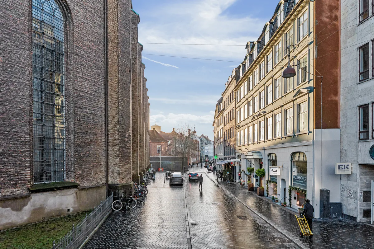 Regnvejrsdag med mennesker og biler på gågaden i København, sammen med en række butikker og en kirke