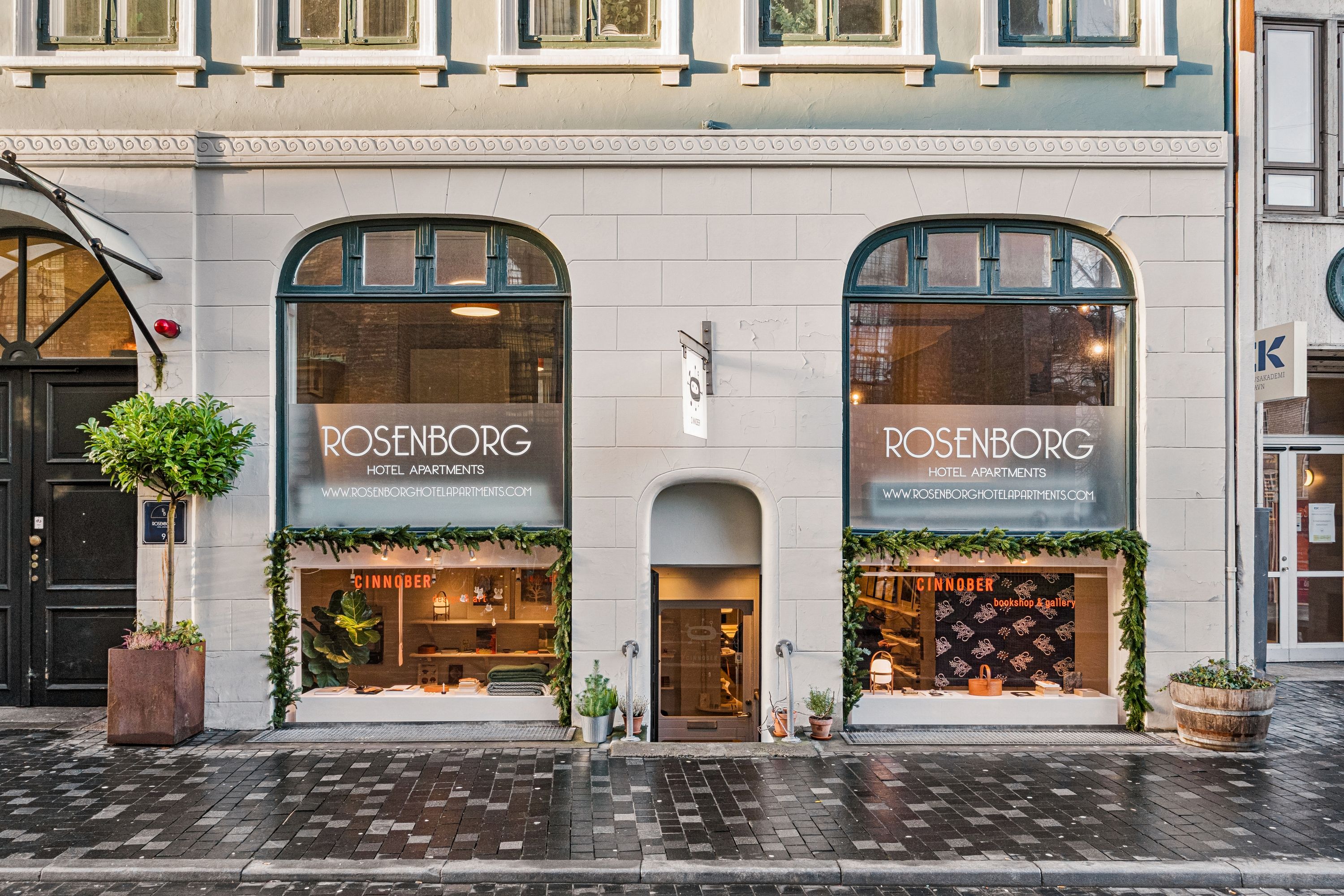 Butik til leje i første sal med udsigt til Landemærket 9 i København K. Vinduesvisning med plantager og smykker i udsigten. Døre og vinduer er udsmykket med lysekroner og kranse.