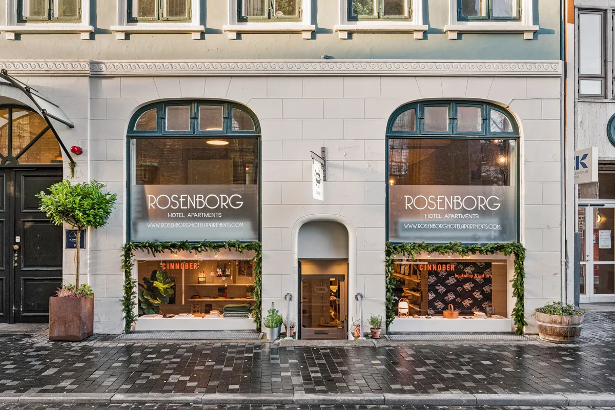 Butik til leje i første sal med udsigt til Landemærket 9 i København K. Vinduesvisning med plantager og smykker i udsigten. Døre og vinduer er udsmykket med lysekroner og kranse.
